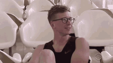 a man wearing glasses sits in a row of white seats