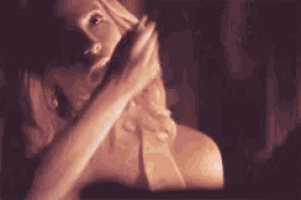 a woman in a bra is covering her mouth with her hands in a dark room .