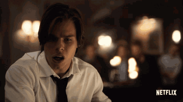 a man in a white shirt and black tie is sitting in front of a netflix logo