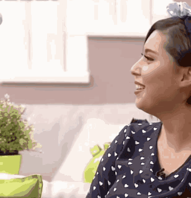 a woman wearing a blue and white polka dot shirt smiles while sitting on a couch