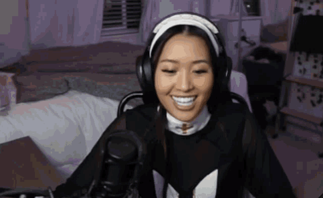 a woman wearing headphones and a headband is sitting in front of a microphone and smiling .