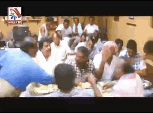 a group of people are gathered around a table with a tv logo on the bottom right corner