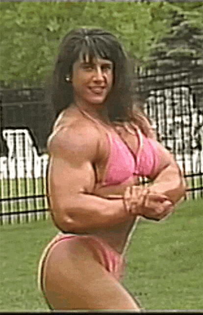 a very muscular woman in a pink bikini is posing with her arms crossed