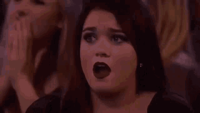 a woman is covering her mouth with her hand while sitting in a crowd of people .