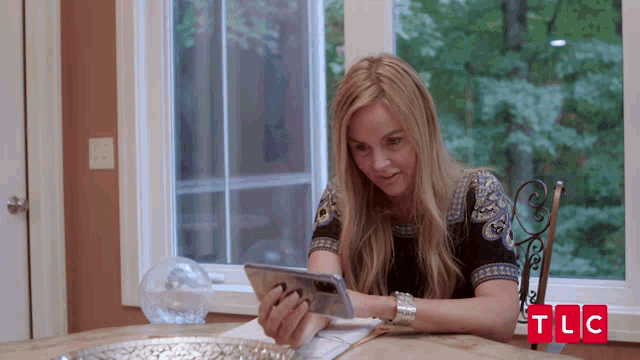 a woman sits at a table looking at a cell phone with tlc written in red