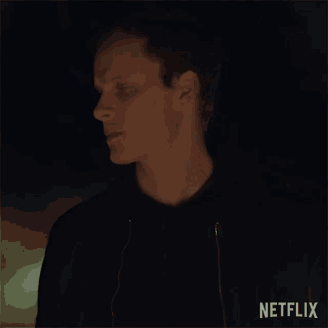 a man in a black hoodie is standing in the dark and looking at something .