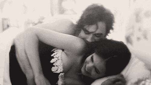 a black and white photo of a man and a woman hugging each other in bed .