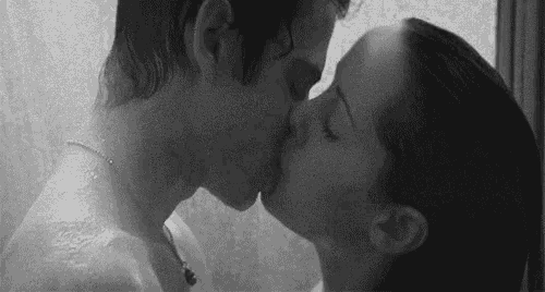 a black and white photo of a man and woman kissing in the shower .