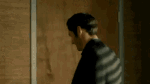 a man in a black suit is standing in front of a wooden door .