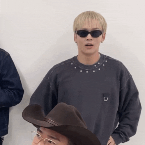 a man wearing sunglasses and a cowboy hat stands next to another man wearing glasses