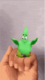 a person is holding a green patrick star figurine