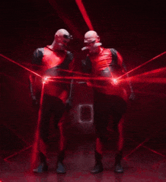 two people are walking in a dark room with red lights behind them .