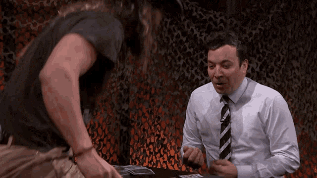 a man in a white shirt and tie is talking to another man in a black shirt