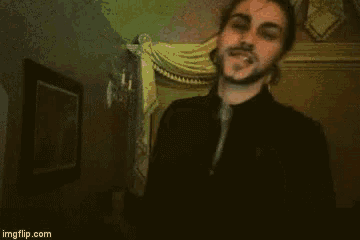 a man with a beard and piercings in his ears is standing in a dark room .