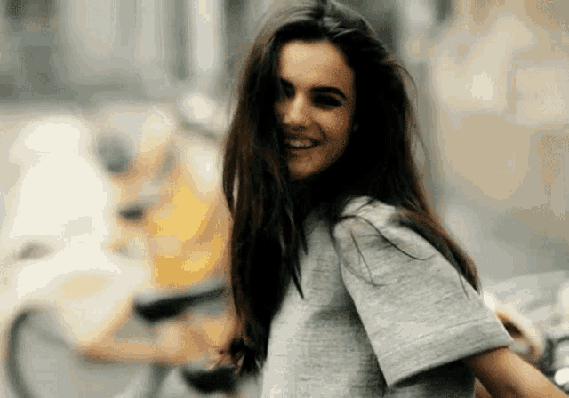 a woman with long hair wearing a grey shirt smiles