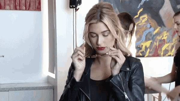 a woman wearing a leather jacket is adjusting her sunglasses