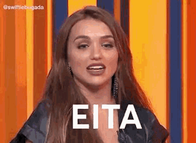 a woman with long hair is standing in front of a yellow wall and says eita .