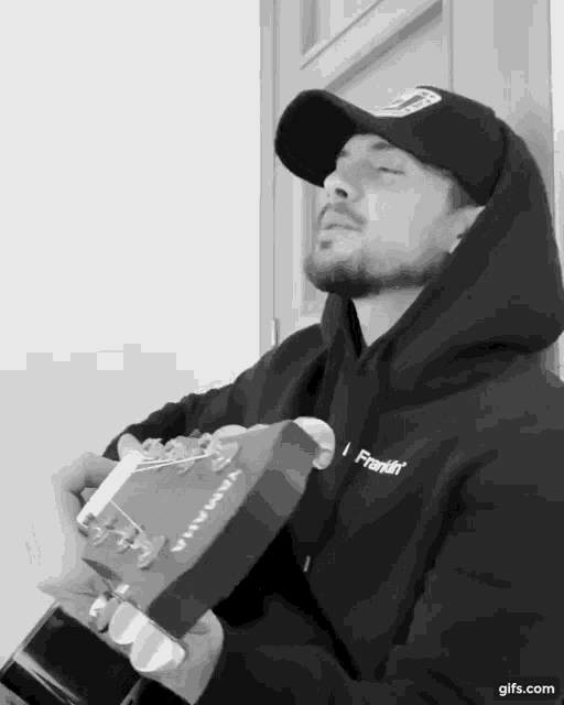 a man wearing a franklin hoodie plays a guitar