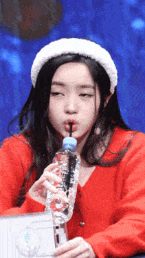 a girl in a red sweater drinking from a bottle with a straw