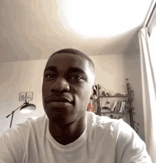 a man in a white shirt is looking at the camera with a bookshelf in the background .