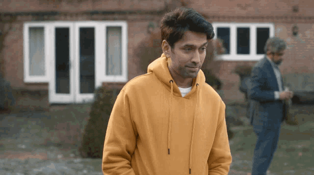 a man wearing a yellow hoodie stands in front of a brick building