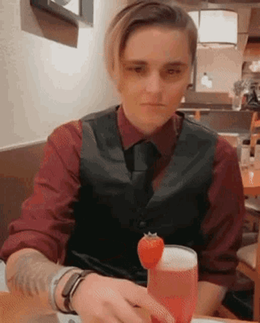 a man in a vest and tie is sitting at a table with a glass of wine and a strawberry on top of it