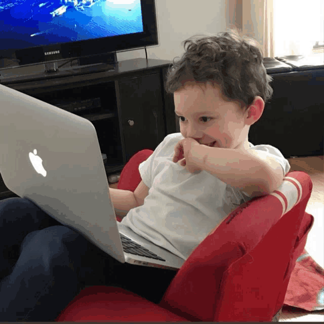 a young boy sits in a red chair with an apple laptop