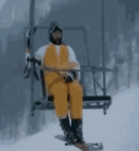 a man in yellow overalls is sitting on a ski lift