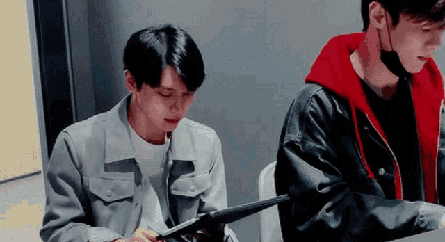 a man in a red hoodie is sitting next to another man in a gray jacket .