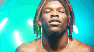 a shirtless man with dreadlocks and a necklace on his neck is looking at the camera .