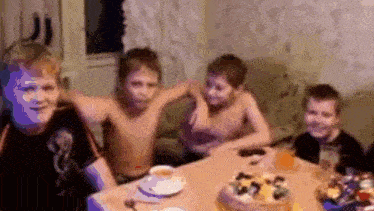 a group of young boys are sitting around a table with a cake .