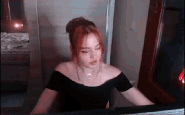 a woman in a black off the shoulder top is sitting in front of a fireplace .