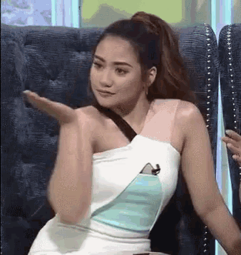 a woman in a white and blue dress is sitting in a chair with her hand outstretched .