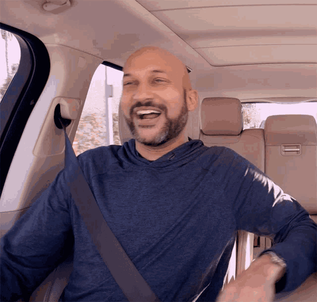a man wearing a blue shirt and a seat belt is laughing in a car