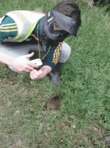 a man wearing a paintball mask looks at a small animal