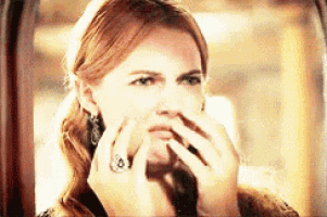 a woman is covering her nose with her hands while looking out a window .