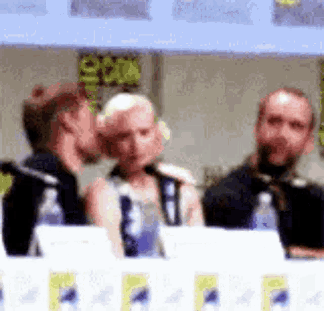 a man is whispering into a woman 's ear at a comic con panel .