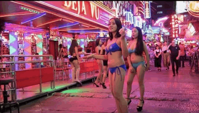 a group of women in bikinis are walking down a street in front of a bar .