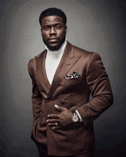 a man wearing a brown suit and a white turtleneck has his hand in his pocket