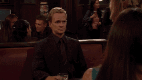 a man in a suit sits at a table with a glass of whiskey and a bowl of food