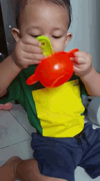 a baby wearing a yellow and green shirt is drinking from an orange cup