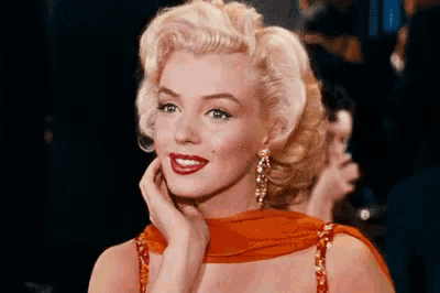 marilyn monroe is wearing a red dress and earrings and holding her hand to her face .