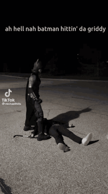 a man in a batman costume is standing next to a man laying on the ground ..