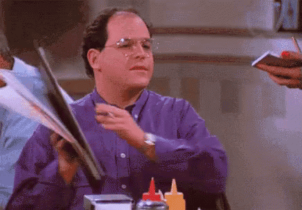 a man in a purple shirt is sitting at a table holding a menu and a cell phone .