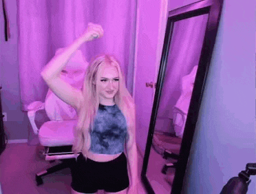 a woman in a crop top and shorts is standing in front of a mirror in a room .