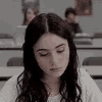 a young woman is sitting at a desk in a classroom looking down .