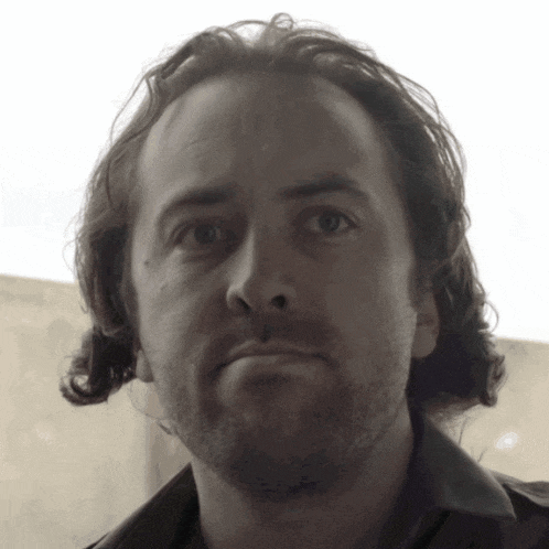 a man with long hair and a beard looks at the camera with a serious look on his face