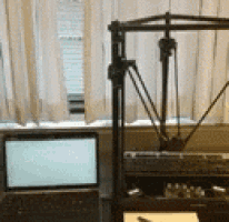 a 3d printer is sitting next to a laptop computer on a desk .