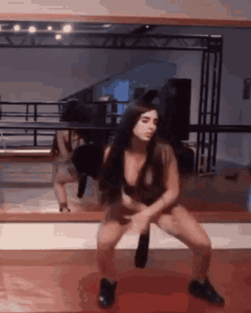 a woman is squatting in front of a mirror in a dance studio .