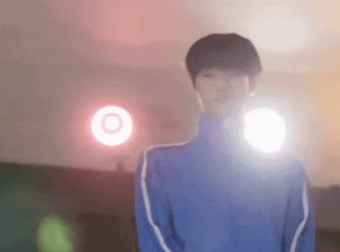 a young man in a blue jacket is standing in front of a red light .
